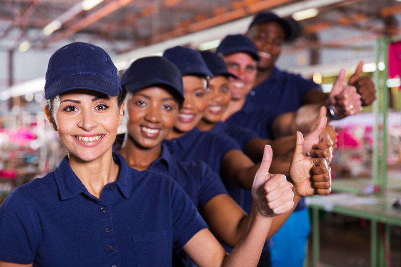 a group of manufacturing employees smiling and giving the thumbs up sign